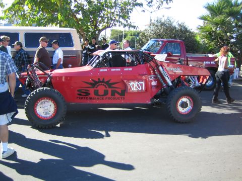 1990 Ford Bronco - red tube-frame off-road race buggy lettered SUN Performance Products and numbered 1207 sits on a street as people stand nearby.