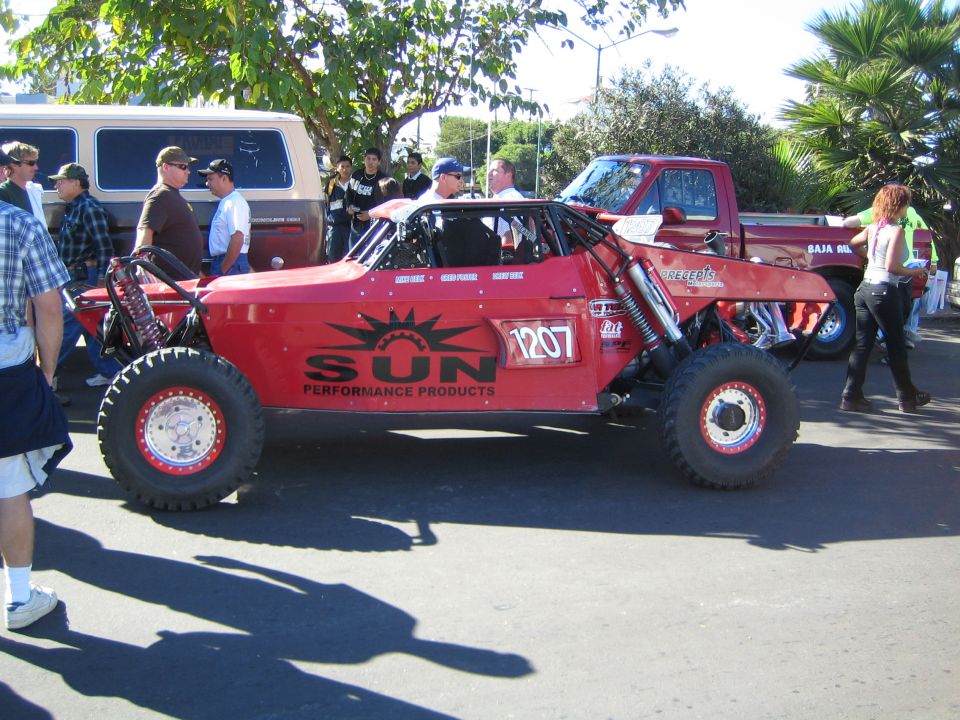 Red off-road race buggy with SUN Performance Products graphics and number 1207 on a street