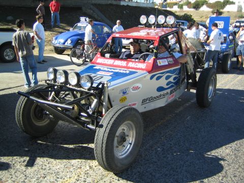 1990 Ford Bronco - red, white and blue tube-frame off-road buggy lettered Becker Bros Racing and BFGoodrich, with a front light bar, sits on a paved lot.