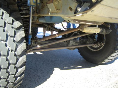 1990 Ford Bronco - close-up of the undercarriage of a lifted off-road truck, showing the front axle, leaf springs, blue shocks and large off-road tires.