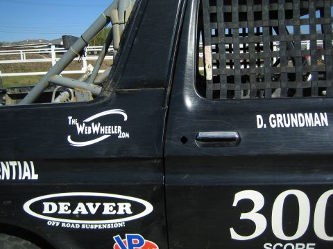 1990 Ford Bronco - Detail of a black off-road race truck's door panel with sponsor decals including DEAVER suspension, race number 300, and the name D. Grundm…