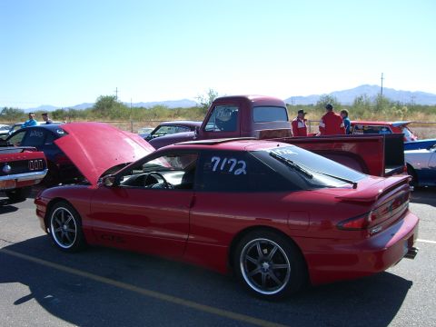 1997 Ford Probe - A red coupe, possibly a Ford Probe, is parked with its hood open at an outdoor event, showing racing numbers on the window.