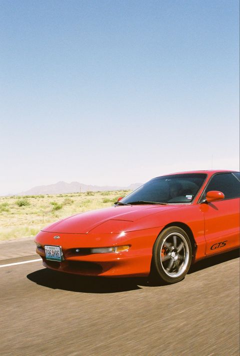 1997 Ford Probe - A red 1997 Ford Probe GTS is captured in a 3/4 front view while driving on a highway under a clear blue sky.