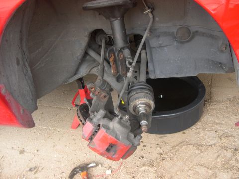 1997 Ford Probe - Front wheel assembly of a red car, showing brake caliper and CV axle, with a drain pan underneath.