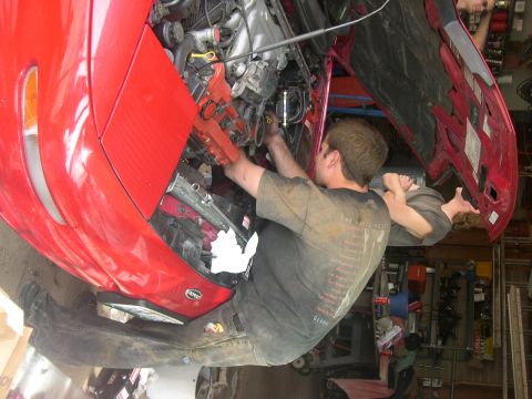 1997 Ford Probe - Mechanic works on the clutch of a red 1997 Ford Probe in the engine bay.