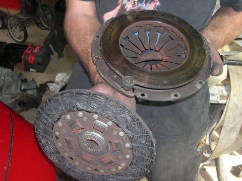 1997 Ford Probe - A person holds a worn clutch disc and pressure plate, likely removed from a vehicle for replacement.