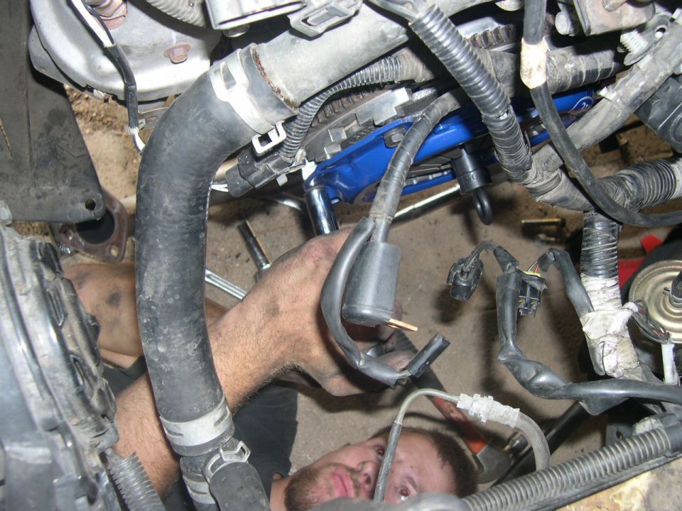 Mechanic working on engine bay, SuperMotors.net logo visible