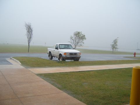 1997 Ford Ranger - A white pickup truck is parked in a grassy area next to a paved lot during a rain shower.