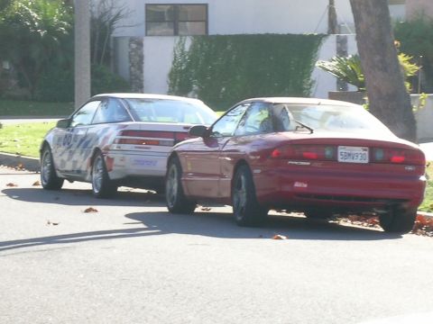1993 Ford Probe - Two cars parked on a street, one is a red 1993 Ford Probe and the other is a white car with racing decals.