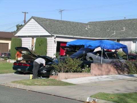 1993 Ford Probe - Two people attend to vehicles in a residential driveway, one with its hood open and another with its trunk ajar.