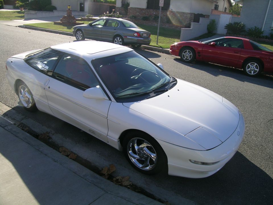White 1993 Ford Probe parked on street, red Pontiac Firebird and gray sedan in background