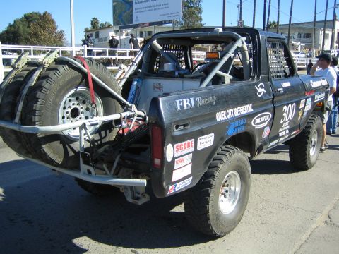 1990 Ford Bronco - black off-road race truck numbered 300 marked FBI Racing and River City Differential, fitted with a roll cage and rear-mounted spare tires.