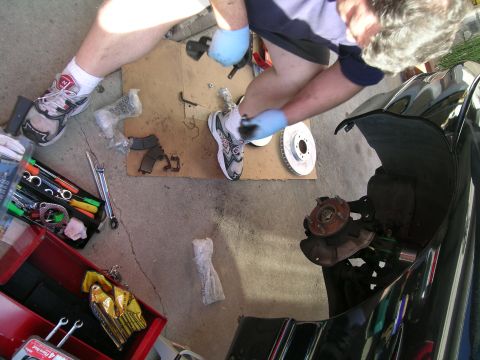 1993 Ford Probe - Mechanic performing brake maintenance on a vehicle, with tools and parts laid out on the ground.