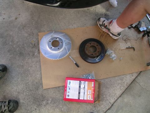 1993 Ford Probe - A new slotted brake rotor and an old rotor are laid out on cardboard, along with hardware and a marker, ready for installation.