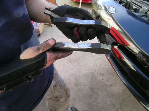 1993 Ford Probe - Hands hold new brake pads, ready for installation on a dark blue vehicle.