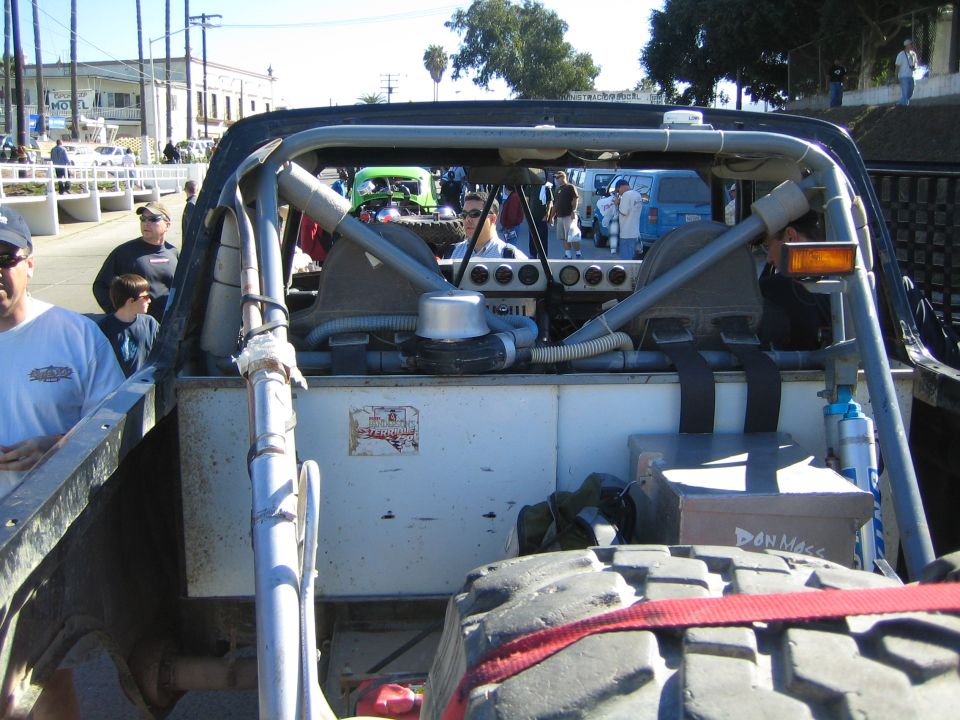 Engine bay and roll cage of off-road race truck viewed from front with crowd behind