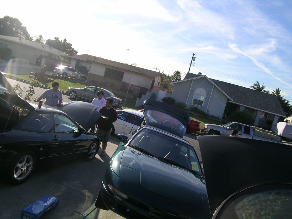 people gathered around cars with hoods open, one car is dark green, another is black