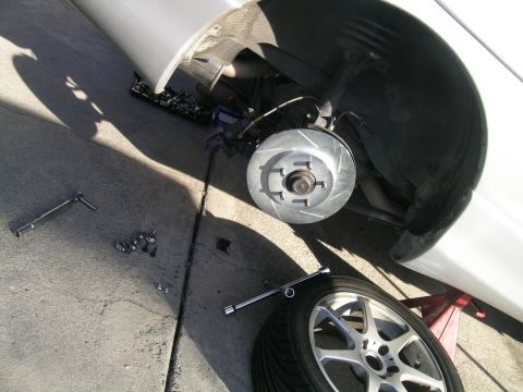 1993 Ford Probe - A car's front wheel assembly is shown with the brake rotor and caliper removed, along with tools and lug nuts scattered on the ground.