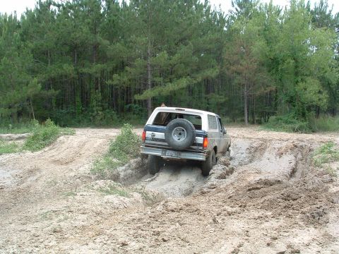 1993 Ford Bronco - A white and blue Ford Bronco navigates a muddy off-road course with a spare tire on the back.