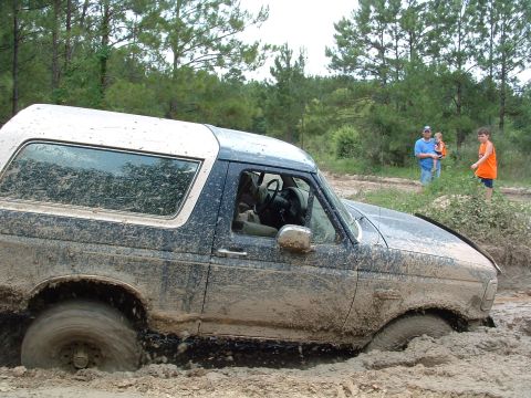 1993 Ford Bronco - A mud-covered 1993 Ford Bronco is stuck deep in the mud, with onlookers in the background.