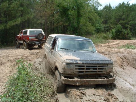 1993 Ford Bronco - Two Ford Broncos navigate a muddy off-road trail, with one vehicle stuck and being pulled.