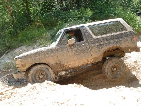 1993 Ford Bronco - This SUV is covered in mud as it navigates a challenging off-road terrain.