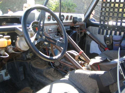 1990 Ford Bronco - Passenger-side view of an off-road race truck cabin showing the steering wheel, gauge cluster, wiring and roll-cage tubing.