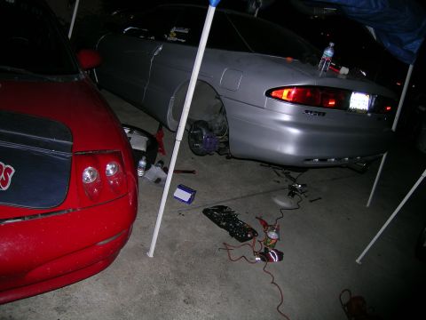 1993 Ford Probe - A silver 1993 Ford Probe is seen with its rear wheel removed, parked next to a red car.