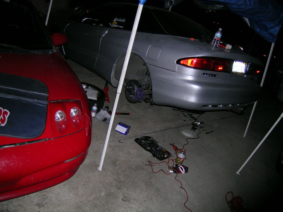 Silver 1993 Ford Probe rear with wheel removed, red car front