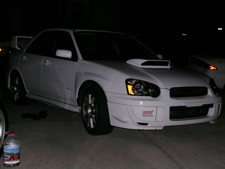 White Subaru WRX STI sedan parked at night, showing front bumper with STI badge