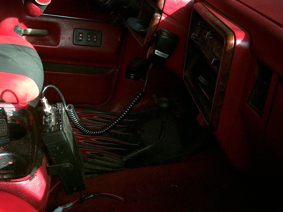 Interior shot of a vehicle's dashboard with a CB radio mounted on the center console. A microphone hangs from the radio