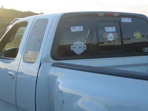 1990 Ford Bronco - bed and rear cab of a light Ford pickup display TWW #300 stickers and a Harley-Davidson decal on the glass.