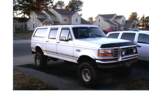 1992 Ford C-150 (Centurion Conversions) - White extended SUV with lifted suspension and aftermarket wheels parked on a street with houses in the background.