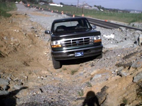 1996 Ford Bronco - A dark green Ford Bronco navigates a rocky, off-road path near a construction site.