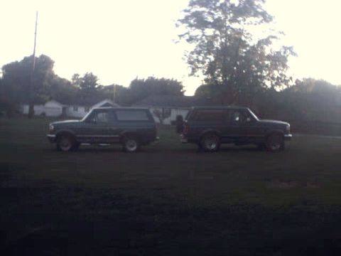 1996 Ford Bronco - Two 1996 Ford Broncos are parked side-by-side on a grassy area with houses and trees in the background.