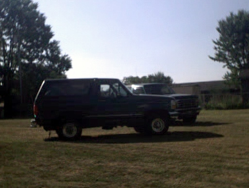 Dark blue Ford Bronco parked on grass, side view. Another vehicle is behind it
