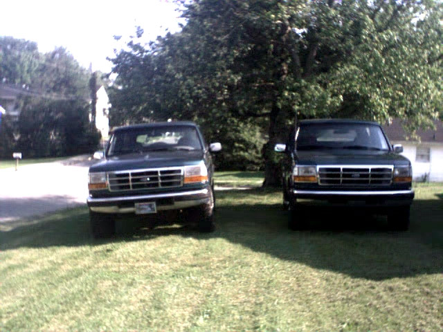 Two dark 1990s Ford trucks parked front-facing on a grass lawn