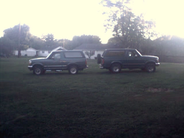 Two dark green Ford Broncos parked on a grassy field during the day