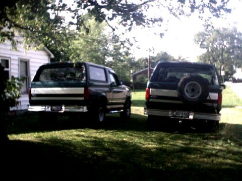 1996 Ford Bronco - Two SUVs are parked in a yard on a sunny day, with trees and a house in the background.