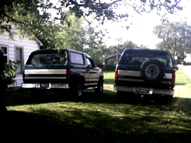 Two dark green SUVs with silver trim parked in a grassy yard. One has a spare tire mounted on the rear door