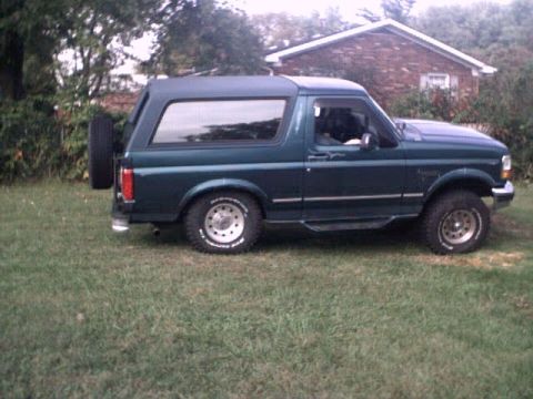 1996 Ford Bronco - A dark green Ford Bronco is parked on a grassy lawn with a house in the background.