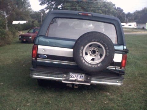 1996 Ford Bronco - A dark green Ford Bronco is parked on grass with another red vehicle in the background.