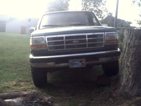 1996 Ford Bronco - Front view of a green Ford Bronco, likely from the early to mid-1990s, parked in a grassy area next to a tree.