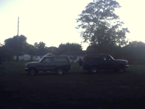 1996 Ford Bronco - Two Ford Broncos, a dark green and a dark blue model, are parked next to each other in a grassy area.