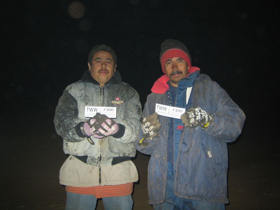 Two mustached men in heavy jackets at night holding small TWW #300 cards for the camera