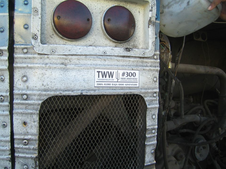 Close-up of a weathered bus rear with two round tail lights, mesh grille and a TWW #300 sticker