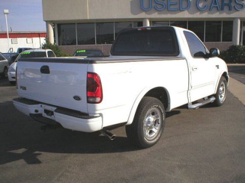 2003 Ford F-150 - A white 2003 Ford F-150 pickup truck is shown from the rear 3/4 angle in front of a dealership.