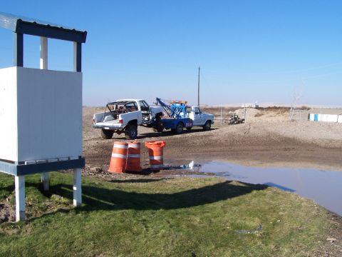 1979 Ford Bronco - A tow truck transports a white pickup truck with a roll cage across a dirt area.