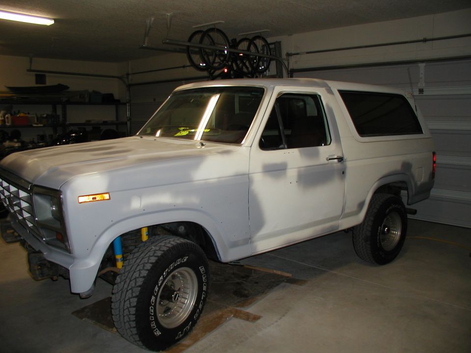 White 1986 Ford Bronco in a garage, prepped for paint, with bikes on roof rack