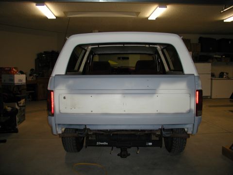 1986 Ford Bronco - Rear view of a 1986 Ford Bronco undergoing body work, showing primer gray panels and a white camper shell.